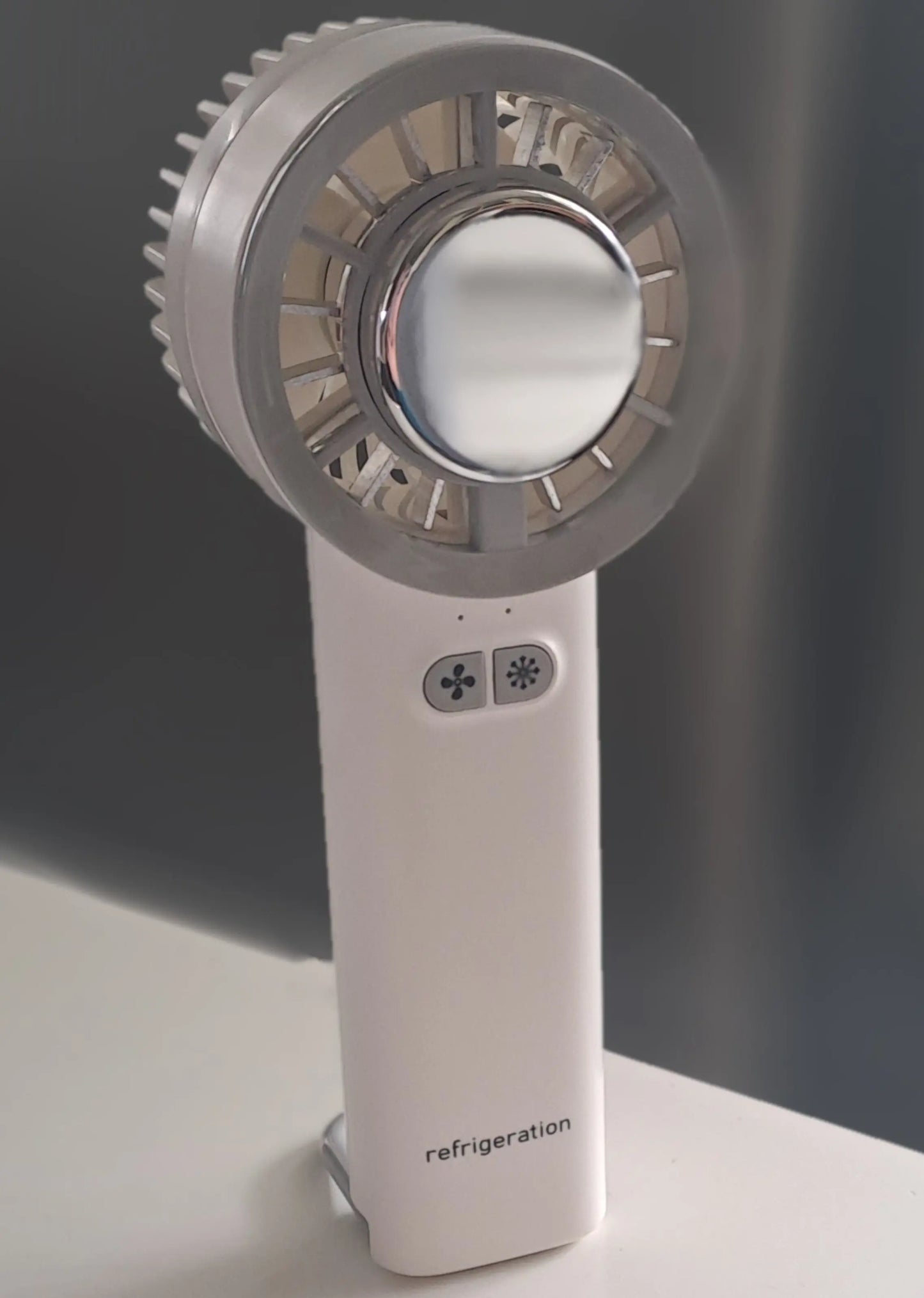 Kraftig, håndholdt hvit vifte med kjøleknapp og stilrent design, plassert på en lys overflate mot mørk bakgrunn.