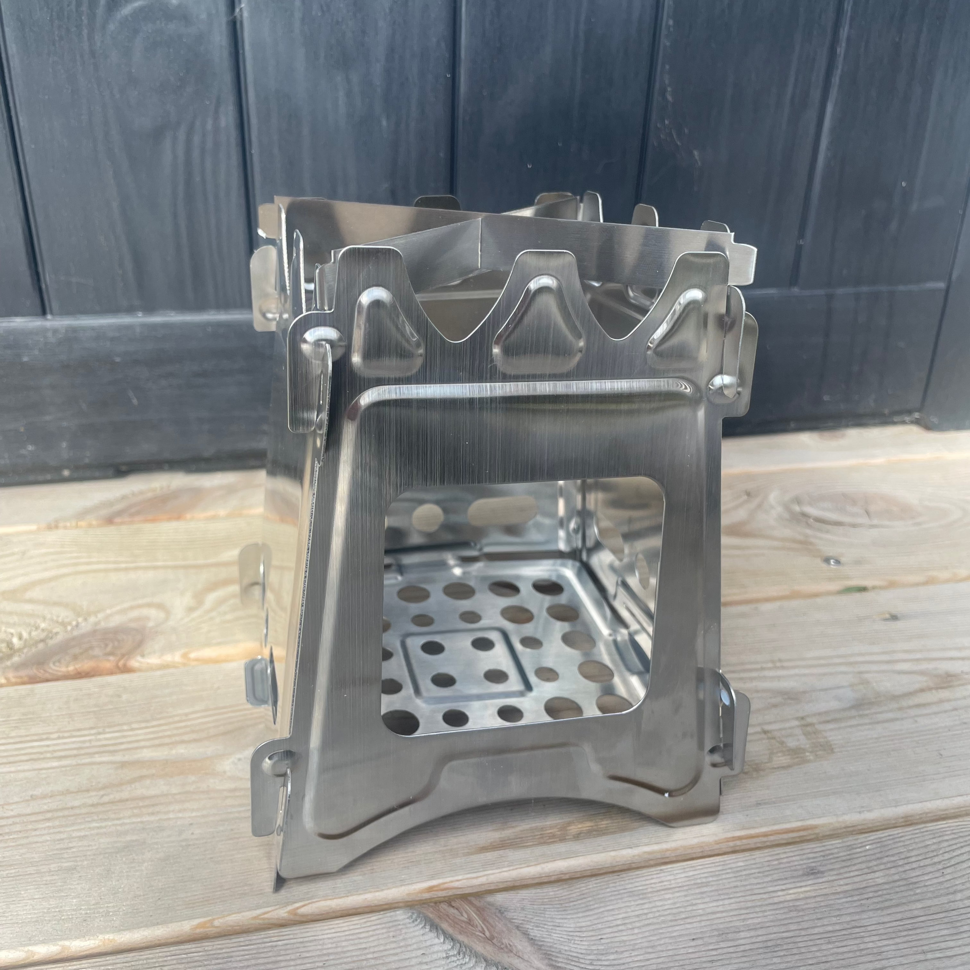 Miljøvennlig kvistbrenner i rustfritt stål plassert utendørs, klar til bruk for matlaging over åpen ild. Kompakt og slitesterk design, ideell for tur og camping.