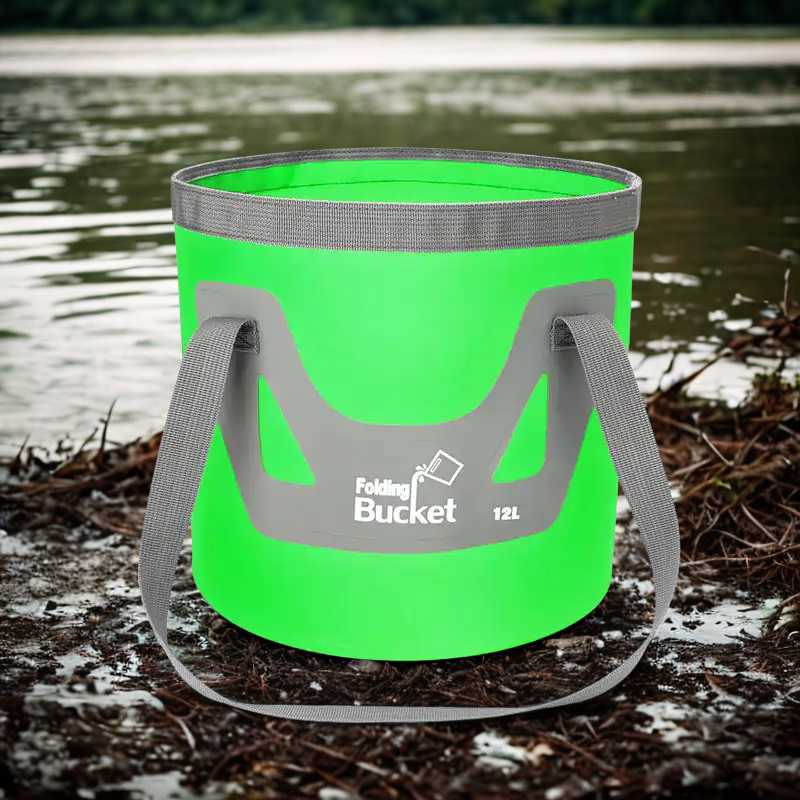 Grønn sammenleggbar bøtte med grå bærestropper plassert ved vannkanten.