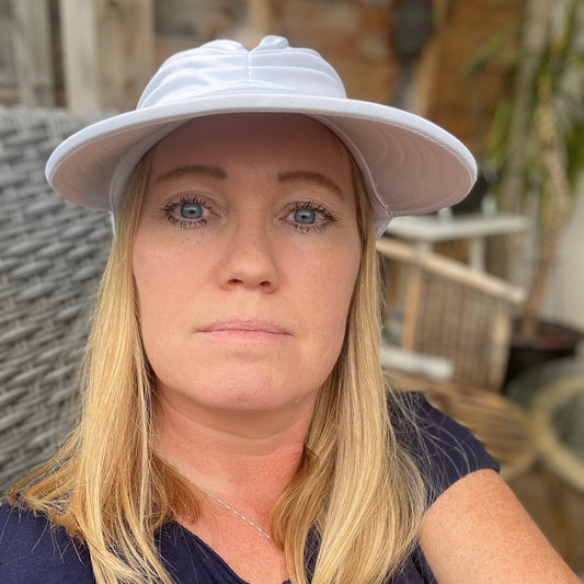 Kvinne med blondt hår iført trendy hvit solhatt med bred brem, perfekt for solfylte dager. Hatten kombinerer stil og solbeskyttelse, ideell for tur, strand og hagebruk.

