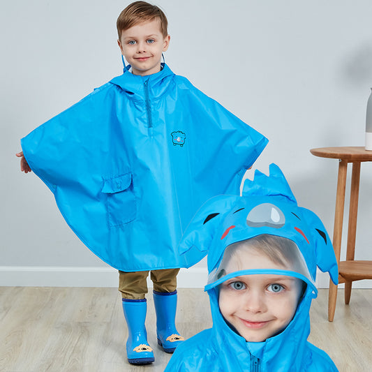 Barn med blå regnponcho og matchende regnstøvler smiler inn i kameraet. Ponchoen har hette med morsomt dyredesign og gir full beskyttelse mot regn.