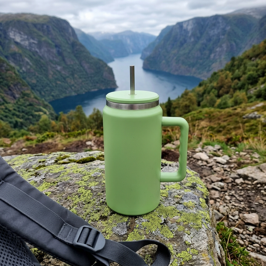 Grønn termokopp med sugerør ute i naturen på tur