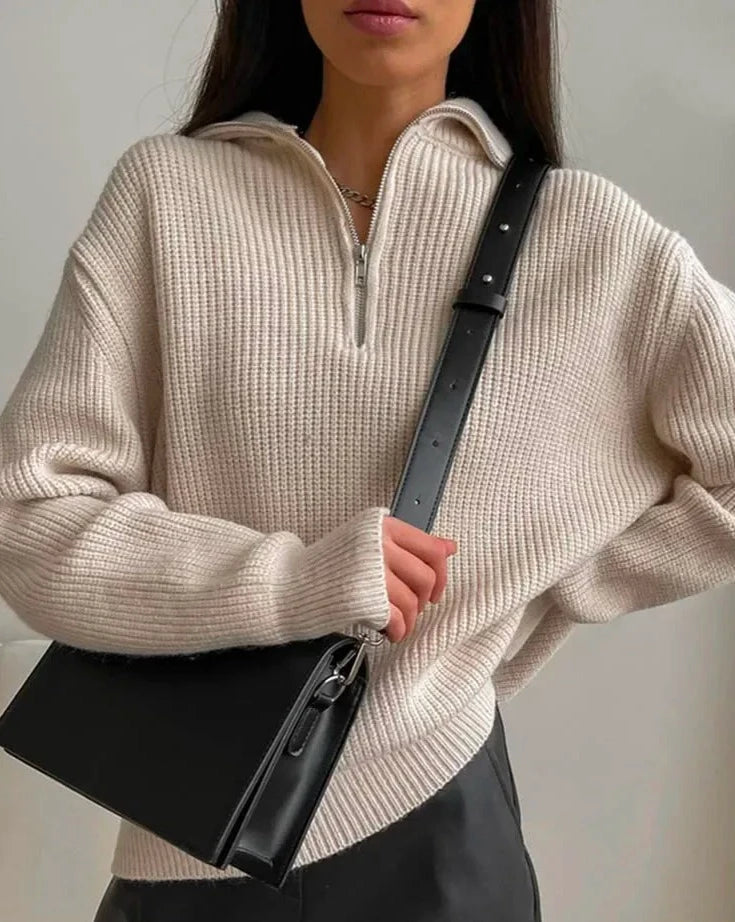 En beige genser med glidelås. Genseren har en klassisk passform og ribbestrikkede detaljer ved ermer og hals. Glidelåsen går fra halsen ned til brystet, noe som gir mulighet for justering av kragen. Stoffet er mykt og behagelig, ideelt for både hverdagsbruk og avslappende øyeblikk.