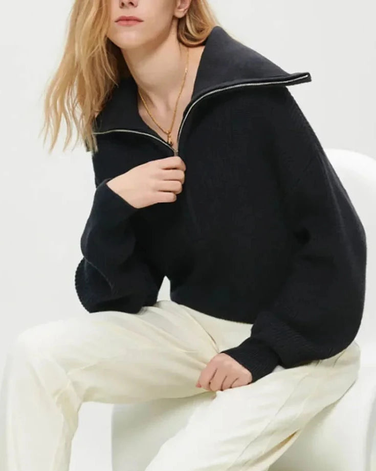 En svart genser med glidelås. Genseren har en klassisk passform og ribbestrikkede detaljer ved ermer og hals. Glidelåsen går fra halsen ned til brystet, noe som gir mulighet for justering av kragen. Stoffet er mykt og behagelig, ideelt for både hverdagsbruk og avslappende øyeblikk.